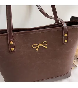 Close-up of dark brown tote bag featuring golden bow detail and metallic rivet accents