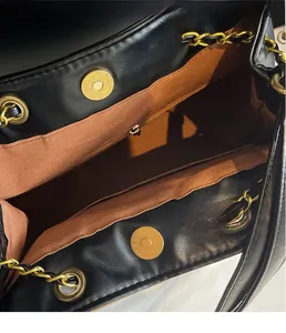 Detail view of gold magnetic buckle, eyelets and leather chain strap on a black bucket bag