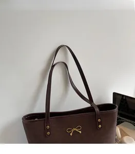 Detail of dark brown tote bag with golden bow and rivet accents for office commute
