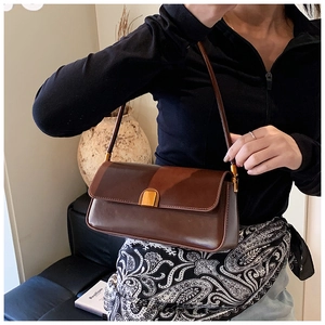 Detail of dark brown leather underarm baguette bag with golden metal clasp on model