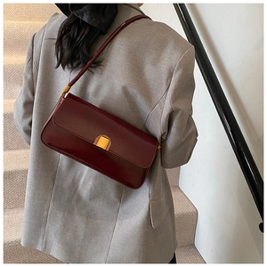 Deep burgundy glossy baguette bag shown as a shoulder style on model with gold buckle