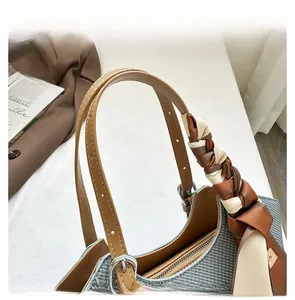 Detail display of brown leather handle with silk scarf on a grey woven handbag