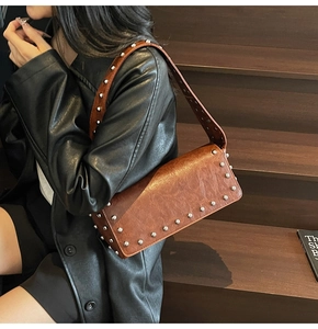 Close-up of brown vintage rectangle shoulder bag with silver studs on a wooden staircase