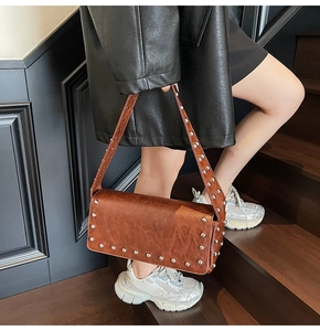 Brown vintage faux leather shoulder bag with silver studs worn by a model on stairs