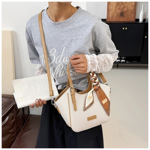 White woven handbag with brown leather trim and decorative scarf detail on the handle