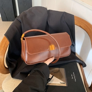 Detailed view of deep brown leather baguette bag with shiny gold-tone hardware and flap