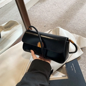 Detail of black glossy faux leather baguette bag with a gold semi-circle buckle