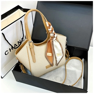 Detail of beige woven tote bag with brown leather handles and decorative silk scarf