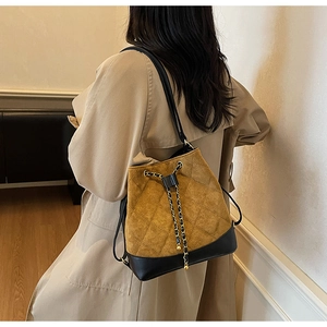 Detail of mustard yellow quilted drawstring bucket bag with black leather base and chain