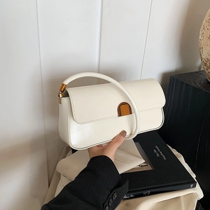 Detail of minimalist cream baguette bag featuring vintage amber magnetic buckle closure
