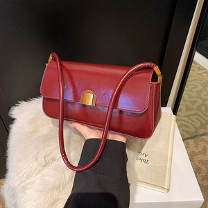 Close-up of a deep red patent leather baguette bag featuring a gold half-moon lock buckle