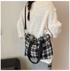 Detail of checkered tote bag with black straps and metal hooks on model shoulder