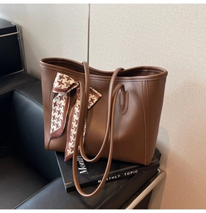 Detailed view of a brown leather tote bag with houndstooth silk scarf and long shoulder straps