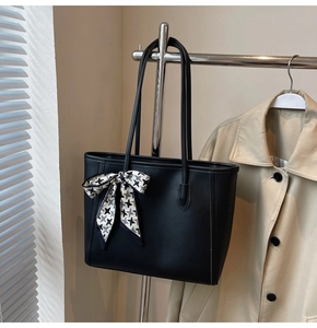 Detail of black tote bag with houndstooth ribbon scarf tied to handle on coat rack