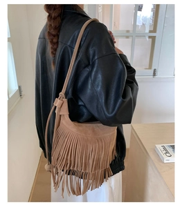 Détail d'un sac hobo en daim camel à franges porté sur une veste en cuir noir