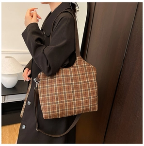 Detailed side view of a brown plaid tote bag with wide shoulder strap on a model