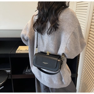 Detail of black leather crossbody bag with woven texture lid and gold metal buckle