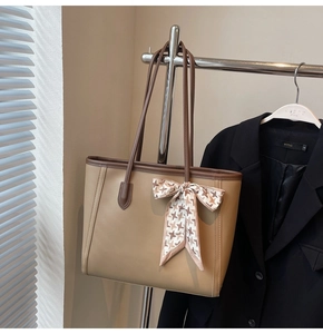 Detail of beige tote bag with dark brown leather trim and houndstooth bow decoration