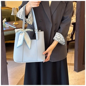 Detail of light blue lychee pattern leather tote bag with decorative silk ribbon on handle