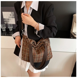 Detail of a brown plaid canvas tote bag with woven handles on a model's shoulder