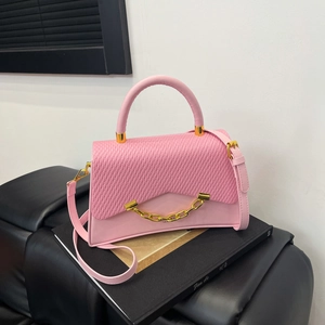 Sac à main rose avec rabat tressé et détail de chaîne dorée sur livres noirs