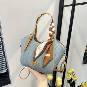 Blue woven handbag with caramel leather handles and silk scarf on home background