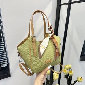 Green woven handbag with brown leather handles and decorative silk scarf in studio setting