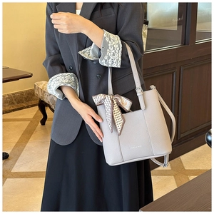 Detail of grey lychee leather bucket bag featuring a brown plaid silk ribbon accent