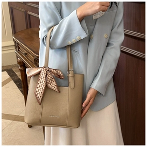 Detail of beige bucket bag with lychee grain texture and a decorative ribbon scarf
