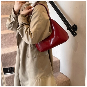 Gros plan d'un sac demi-lune en cuir verni rouge foncé porté avec un trench-coat