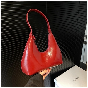 Detail of red patent leather crescent bag featuring a glossy finish and embossed text