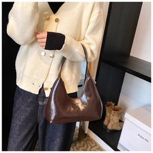 Vue détaillée du sac demi-lune en cuir verni marron foncé porté à l'épaule en décor