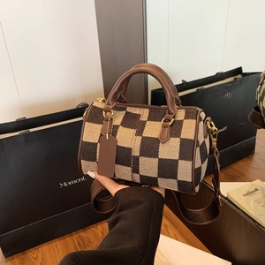 Close-up of checkerboard Boston bag with brown leather handles and woven strap detail