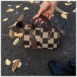 Close-up of checkered canvas bag with leather trim and gold hardware on autumn leaves