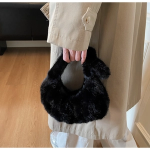 Dettaglio di una borsa a mezzaluna in finta pelliccia nera tenuta su uno sfondo di cappotto beige