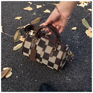 Close-up of checkered canvas Boston bag with leather trim on autumn leaves background