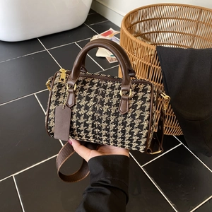 Detail view of houndstooth crossbody bag with brown leather handles and gold hardware