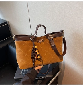 Detail of a brown quilted suede tote bag with wooden bead tassel and gold metal clasp