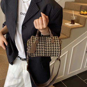 Detail of houndstooth cylinder handbag featuring brown leather handles and woven shoulder strap