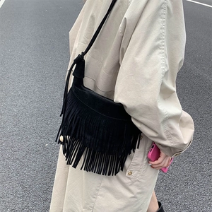Sac bandoulière rétro noir en daim mat avec longues franges porté sur un manteau beige