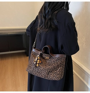 Detail of leopard print tote bag featuring a leather trim and a beaded tassel charm