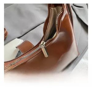 Detail van de zilveren rits en beige voering van een donkerbruine leren schoudertas