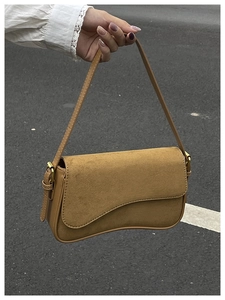 Detail of tan suede shoulder bag featuring vintage saddle lines and bronze metal buckle