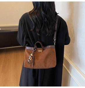 Detailed view of quilted brown suede tote bag with wooden bead charm on a model