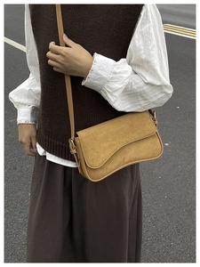 Detail of camel frosted suede underarm bag with wave flap and gold buckle on a model