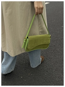 Detail of green suede shoulder bag featuring a unique wavy curve flap and gold buckle