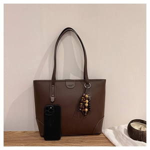 Detailed view of dark brown tote bag with pebble leather texture and beaded tassel charm