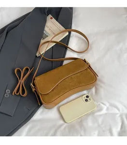 Detailed view of brown matte shoulder bag with suede flap and gold buckle next to a phone