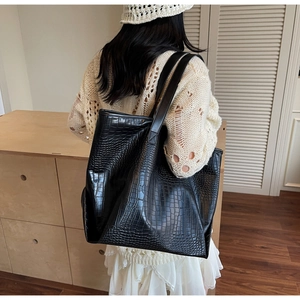 Detail of black faux crocodile leather tote bag worn by model to show large capacity
