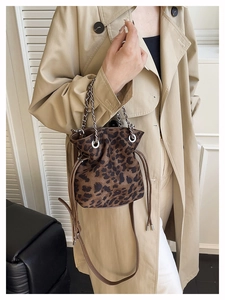 Leopard print bucket bag with metal chain handle and adjustable strap on a beige coat